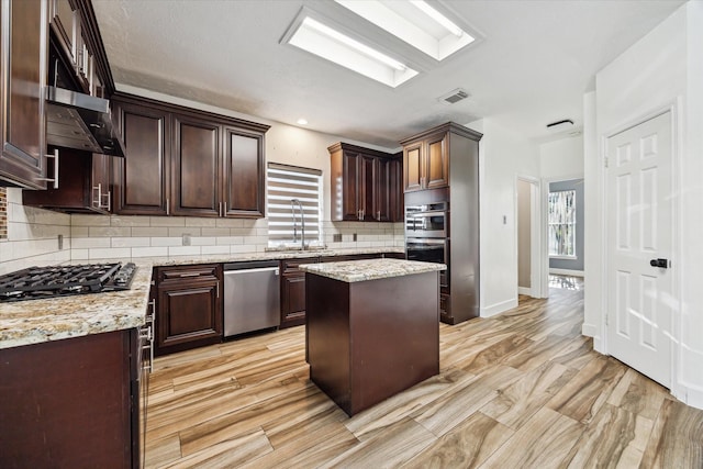 kitchen featuring sink, dark brown cabinets, stainless steel appliances, a center island, and light stone countertops