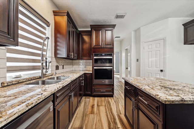 kitchen featuring dark brown cabinetry, light stone countertops, stainless steel appliances, and light hardwood / wood-style floors