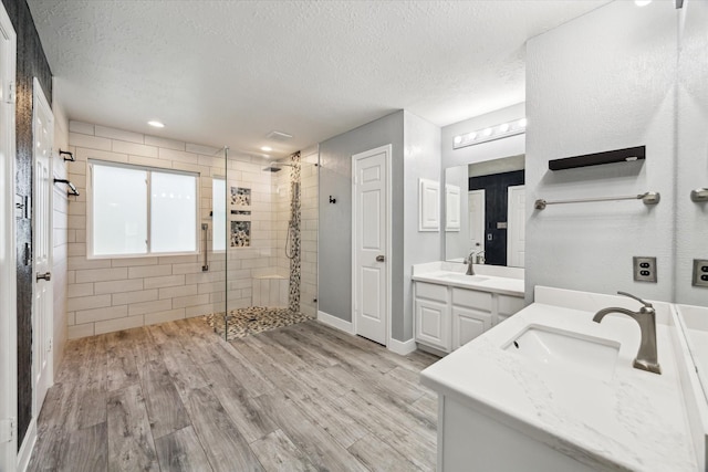 bathroom featuring hardwood / wood-style flooring, vanity, tiled shower, and a textured ceiling