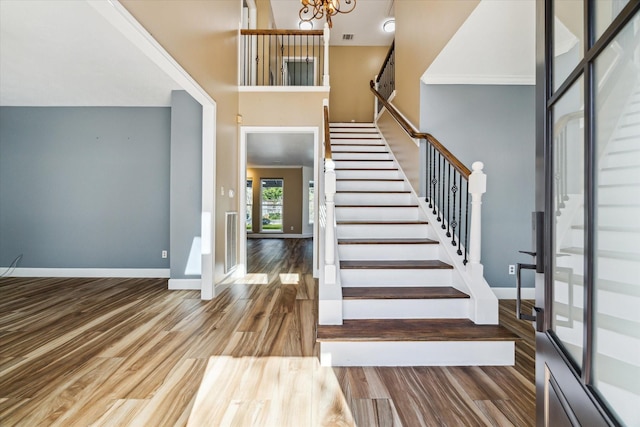 stairway with crown molding, a towering ceiling, hardwood / wood-style floors, and an inviting chandelier