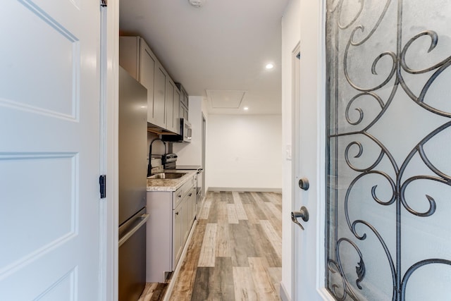 kitchen featuring gray cabinetry, light stone countertops, stainless steel appliances, and light hardwood / wood-style floors