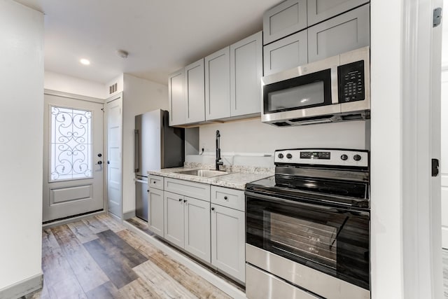 kitchen with sink, gray cabinetry, light stone counters, stainless steel appliances, and light hardwood / wood-style flooring