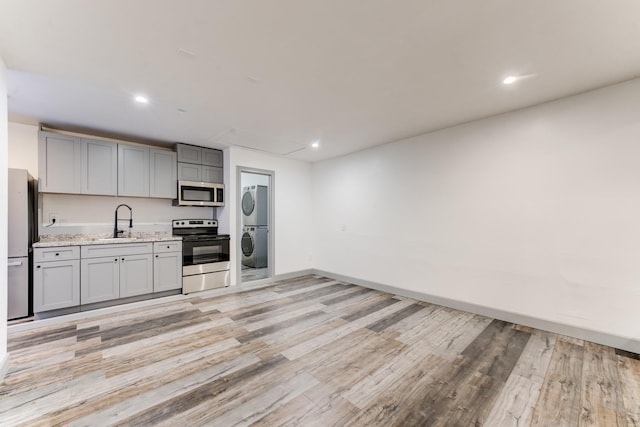 kitchen featuring stacked washer and dryer, appliances with stainless steel finishes, gray cabinetry, and light hardwood / wood-style floors