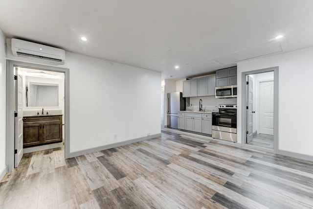 kitchen featuring appliances with stainless steel finishes, sink, gray cabinetry, a wall mounted AC, and light wood-type flooring