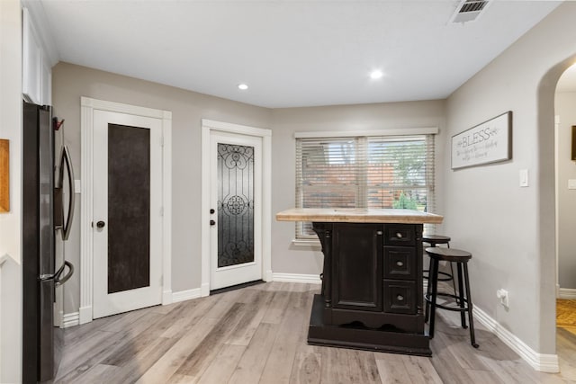 interior space with a kitchen island, stainless steel refrigerator, white cabinetry, a breakfast bar area, and light wood-type flooring