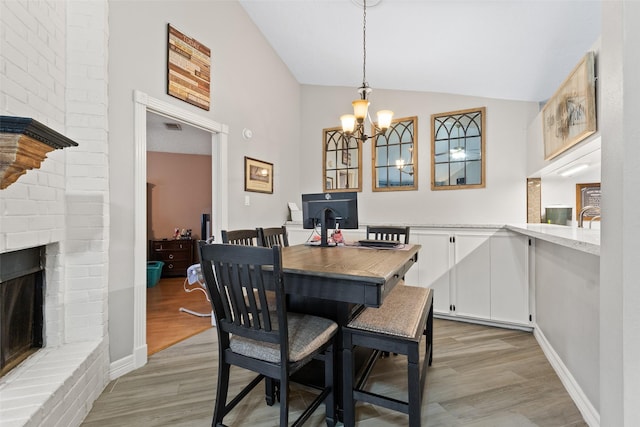 dining space with lofted ceiling, a fireplace, light hardwood / wood-style floors, and an inviting chandelier