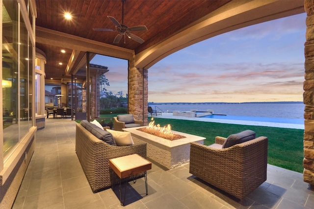 patio terrace at dusk featuring a water view, ceiling fan, and an outdoor living space with a fire pit