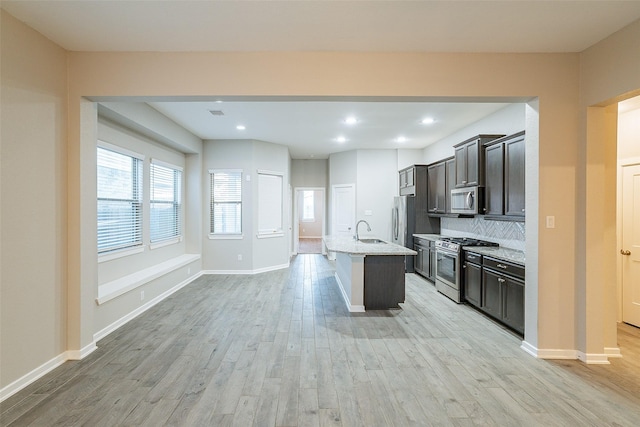 kitchen with appliances with stainless steel finishes, an island with sink, sink, backsplash, and light stone counters