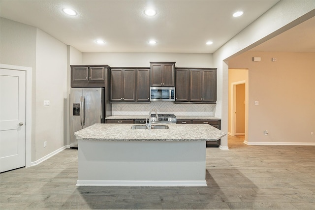 kitchen featuring dark brown cabinetry, sink, light stone counters, appliances with stainless steel finishes, and a kitchen island with sink