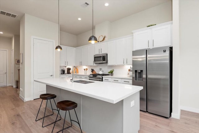 kitchen featuring pendant lighting, sink, appliances with stainless steel finishes, white cabinetry, and an island with sink