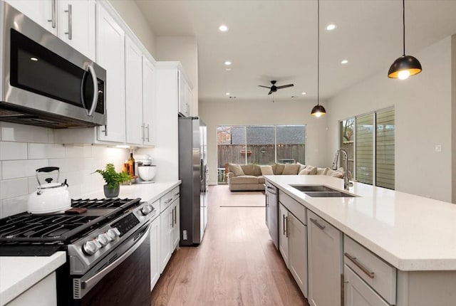 kitchen featuring pendant lighting, sink, appliances with stainless steel finishes, white cabinetry, and an island with sink