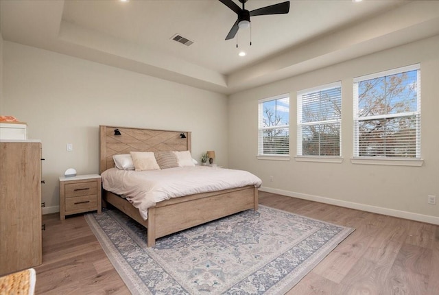 bedroom with ceiling fan, a raised ceiling, and light hardwood / wood-style floors