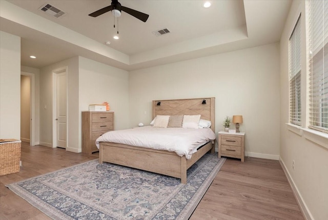 bedroom with multiple windows, light hardwood / wood-style flooring, a raised ceiling, and ceiling fan