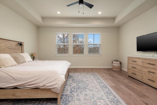 bedroom with hardwood / wood-style flooring, ceiling fan, and a raised ceiling