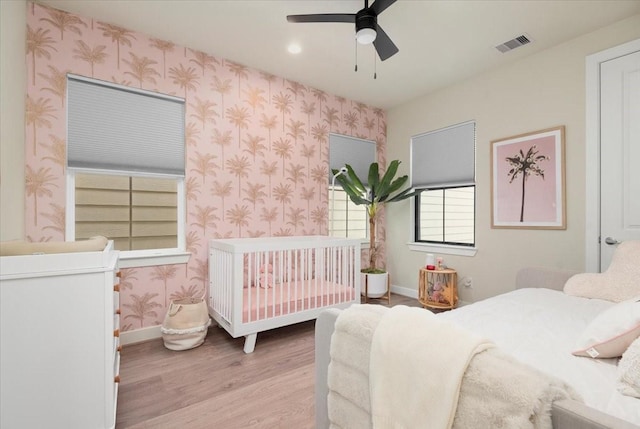 bedroom featuring a crib, light wood-type flooring, and ceiling fan