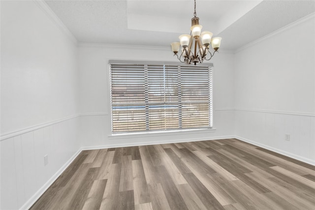 empty room with hardwood / wood-style flooring, ornamental molding, a chandelier, and a tray ceiling