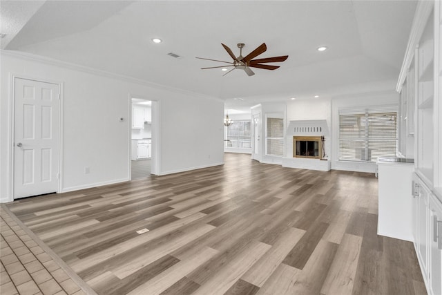 unfurnished living room featuring lofted ceiling, crown molding, a brick fireplace, light wood-type flooring, and ceiling fan with notable chandelier