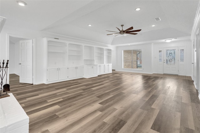 unfurnished living room featuring vaulted ceiling, built in features, ceiling fan, a tray ceiling, and dark wood-type flooring