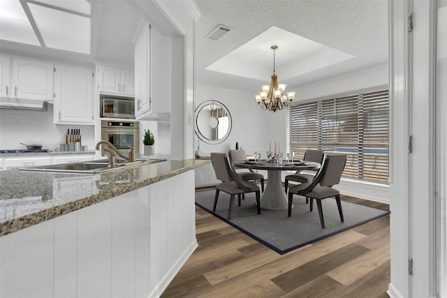 dining area with sink, dark hardwood / wood-style floors, a notable chandelier, a tray ceiling, and ornamental molding