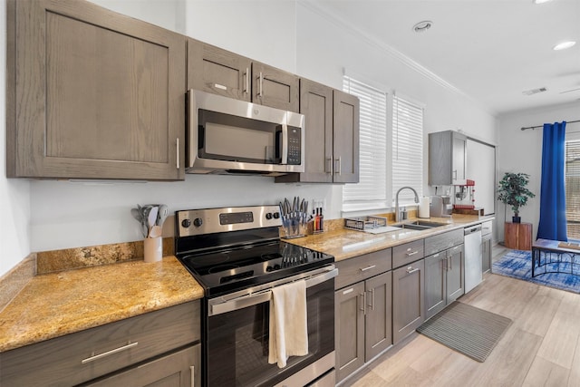 kitchen with sink, ornamental molding, stainless steel appliances, light stone countertops, and light wood-type flooring