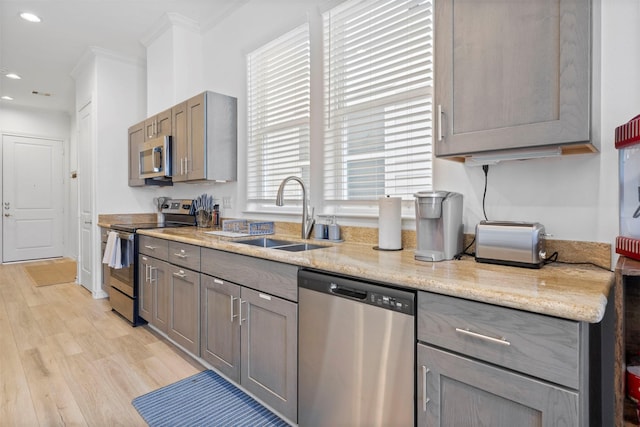 kitchen featuring sink, light hardwood / wood-style flooring, ornamental molding, appliances with stainless steel finishes, and light stone countertops