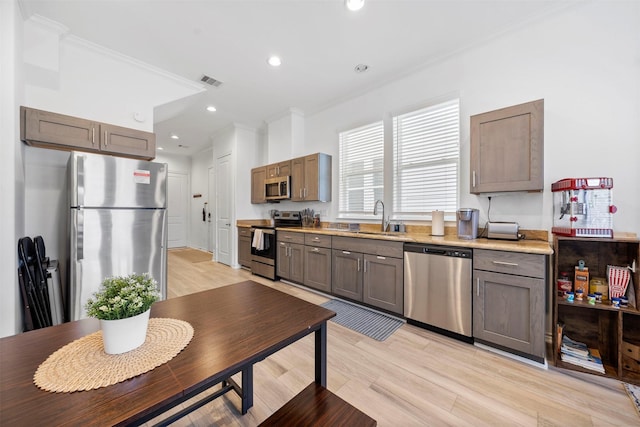 kitchen with sink, light hardwood / wood-style flooring, ornamental molding, and appliances with stainless steel finishes