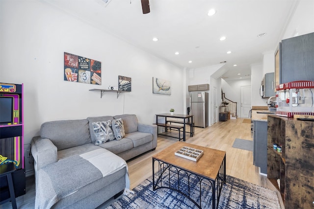 living room featuring ceiling fan, ornamental molding, sink, and light wood-type flooring