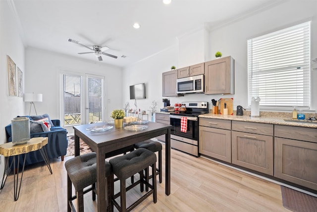 kitchen featuring light stone counters, ceiling fan, stainless steel appliances, crown molding, and light hardwood / wood-style floors