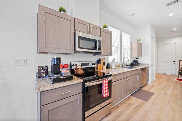 kitchen with sink, crown molding, stainless steel appliances, light stone counters, and light wood-type flooring