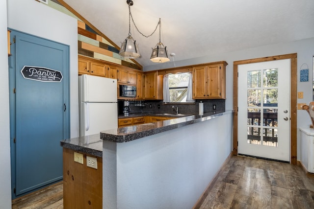 kitchen with vaulted ceiling, black microwave, backsplash, white fridge, and kitchen peninsula