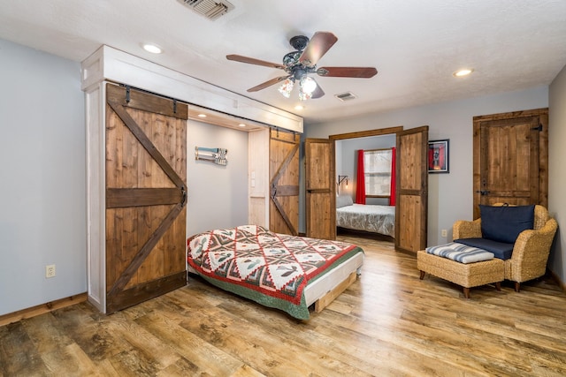 bedroom with wood-type flooring, a barn door, and ceiling fan