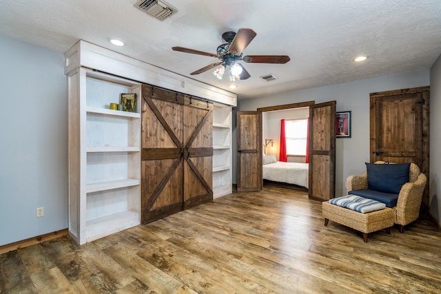 unfurnished room with hardwood / wood-style flooring, ceiling fan, a barn door, and a textured ceiling