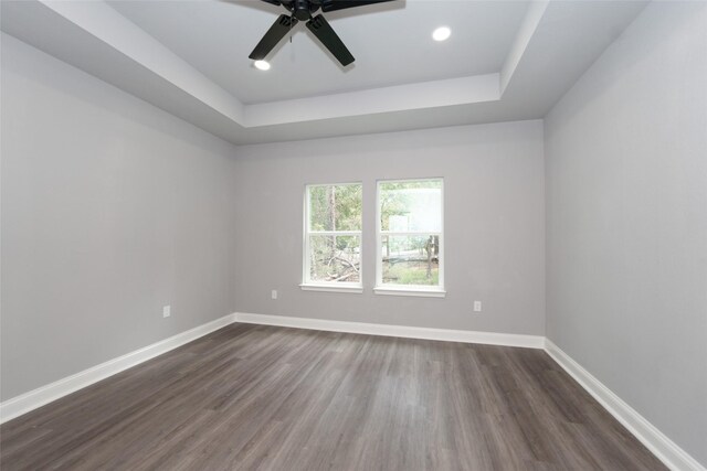 empty room with dark wood-type flooring, ceiling fan, and a tray ceiling