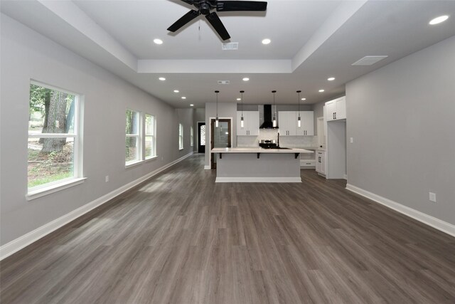 unfurnished living room with dark hardwood / wood-style floors, ceiling fan, and a tray ceiling