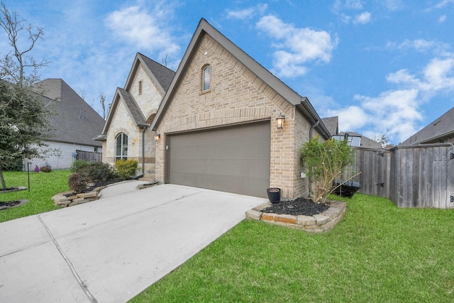 french provincial home with a front yard, fence, concrete driveway, and brick siding