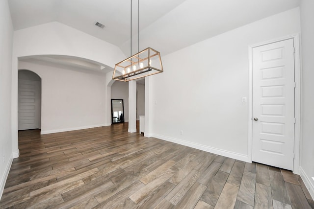 unfurnished dining area with arched walkways, lofted ceiling, wood finished floors, visible vents, and baseboards