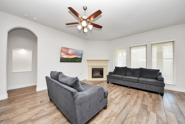 living area featuring light wood-style floors, baseboards, arched walkways, and a glass covered fireplace