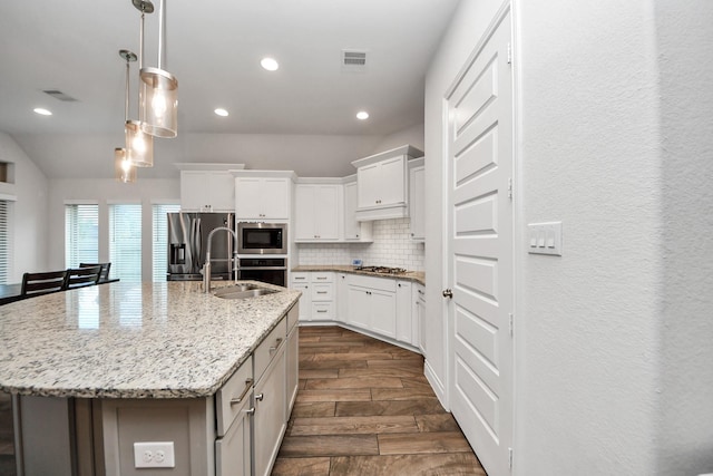 kitchen with stainless steel appliances, white cabinetry, sink, and a center island with sink