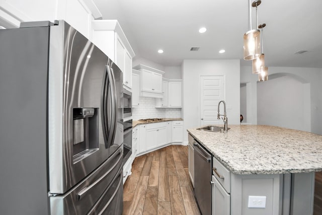 kitchen with appliances with stainless steel finishes, white cabinetry, an island with sink, sink, and light stone countertops