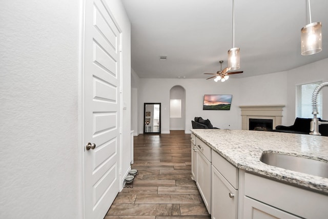 kitchen featuring arched walkways, a ceiling fan, wood tiled floor, a fireplace, and a sink