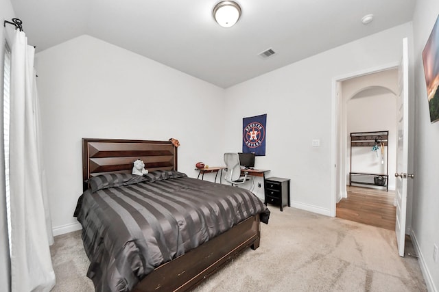 bedroom featuring arched walkways, lofted ceiling, light colored carpet, visible vents, and baseboards