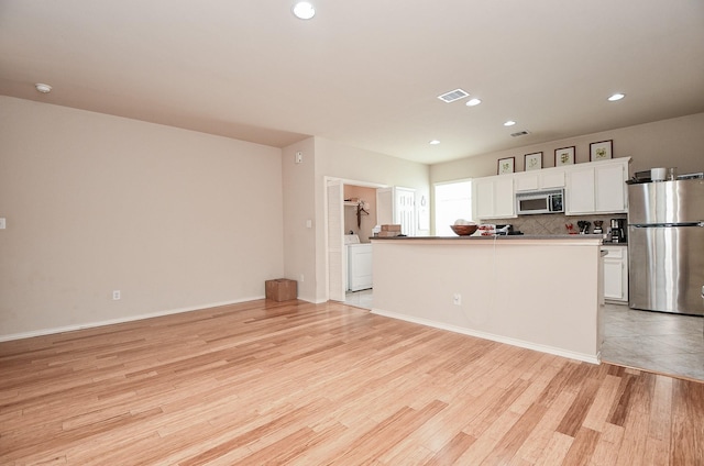 kitchen with tasteful backsplash, white cabinetry, washer / clothes dryer, light hardwood / wood-style floors, and stainless steel appliances