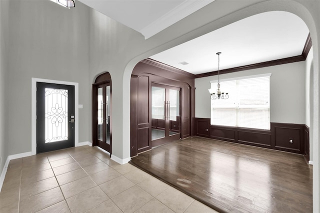 tiled entryway with ornamental molding and a chandelier