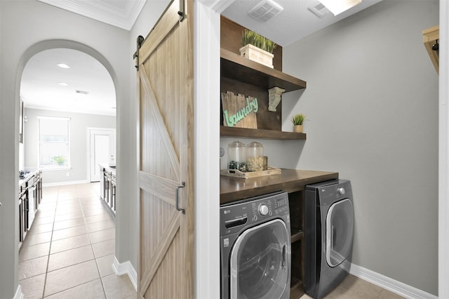 laundry area with light tile patterned flooring, a barn door, washer and dryer, and crown molding