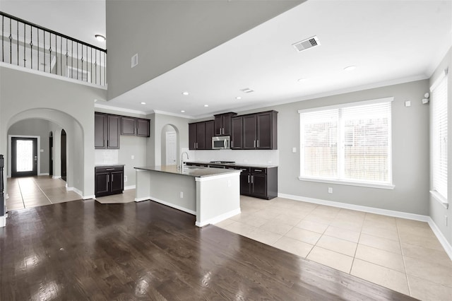 kitchen with dark brown cabinetry, light tile patterned flooring, an island with sink, and appliances with stainless steel finishes