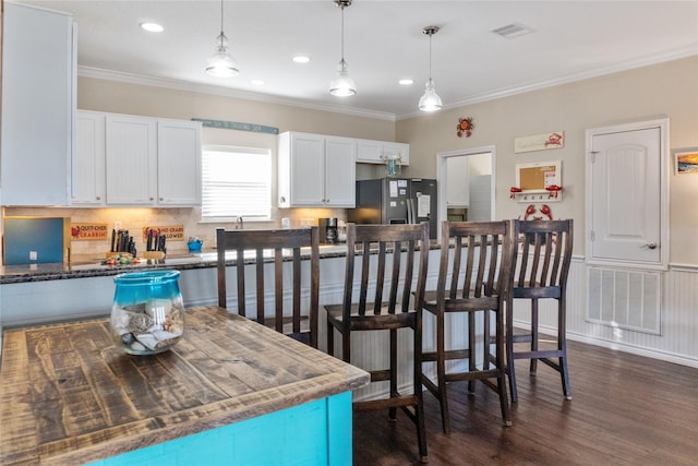 kitchen with dark wood-type flooring, white cabinetry, hanging light fixtures, ornamental molding, and black fridge