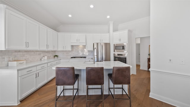 kitchen with a breakfast bar, light stone counters, a center island with sink, stainless steel appliances, and white cabinets