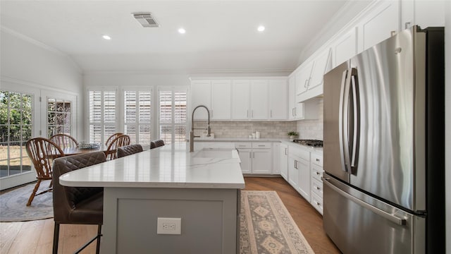 kitchen with appliances with stainless steel finishes, white cabinets, decorative backsplash, a center island, and light stone counters