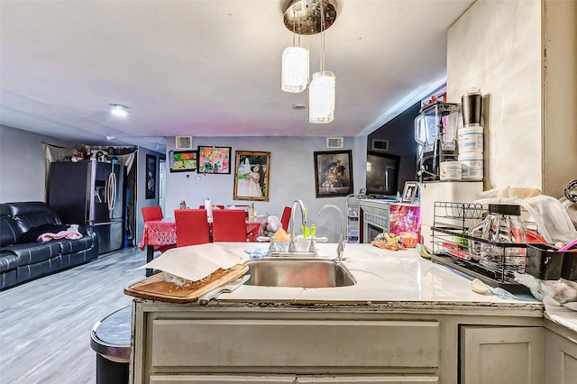 kitchen with cream cabinets, hanging light fixtures, stainless steel refrigerator with ice dispenser, light hardwood / wood-style floors, and sink