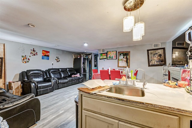 kitchen featuring decorative light fixtures, sink, stainless steel fridge, and light wood-type flooring